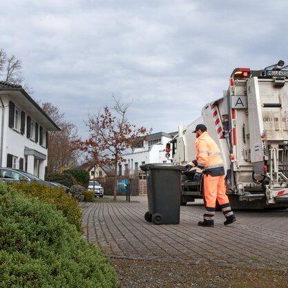 In einer Wohngegend leert ein DBS-Mitarbeiter die Restmülltonne. Er bringt die Tonne vom Entsorgungsfahrzeug zur Hausauffahrt zurück. | © Die Bremer Stadtreinigung