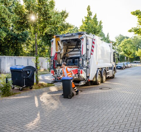 Ein Mitarbeiter der Bremer Stadtreinigung, der Papiertonnen leert. Im Hintergrund steht ein Müllfahrzeug. | © Die Bremer Stadtreinigung