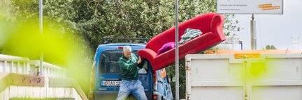 Ein Kunde liefert auf einer Recycling-Station gerade ein Sofa an und entsorgt dieses im Sperrmüll Container.