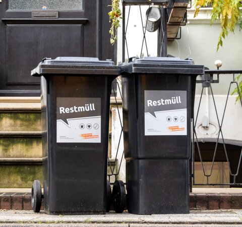Zwei schwarze Abfalltonnen, die vor einem Reihenhaus stehen. Auf beiden Tonnen steht "Restmüll". | © Die Bremer Stadtreinigung